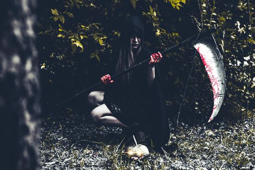 Demon witch sitting and holding reaper in black forest. Halloween day concept.