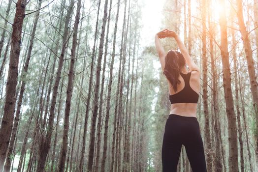 Women stretching arms and breathing fresh air in middle of pinewood forest while exercising. Workouts and Lifestyles concept. Happy life and Healthcare theme. Nature and Outdoors theme. Back view