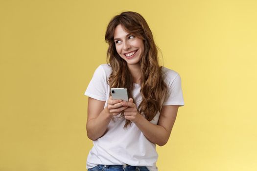 Lovely silly cute flirty girl texting receive romantic lovely gesture look away blushing modest smiling broadly reading bold passionate message stand yellow background joyfully send boyfriend photo