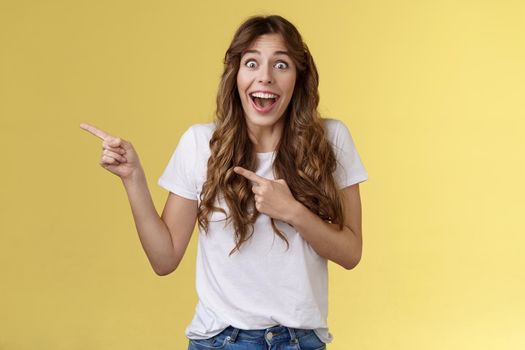 Happy sincere cheerful young surprised woman see celebrity lose speech stare excited unbelievable awesome luck fascinated pointing index fingers left open mouth stunned thrilled yellow background
