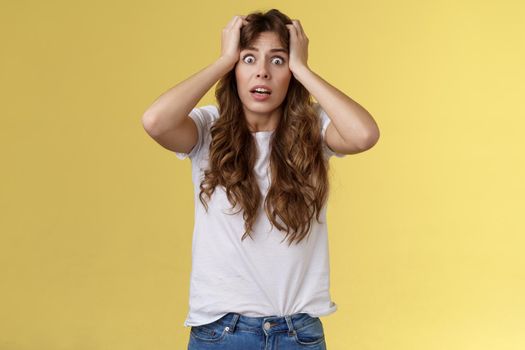 Troubled concerned anxious panicking woman female employee lose control grab head nervously stare camera frustrated scared gasping hopeless puzzled standing yellow background