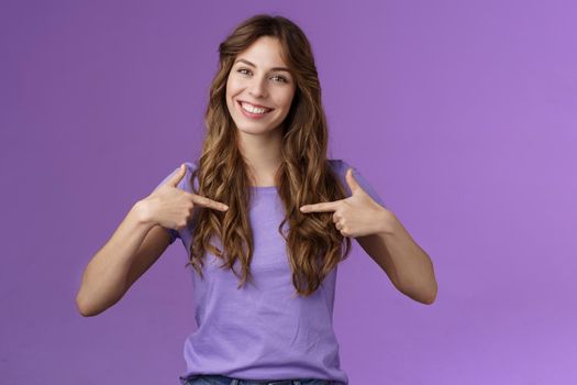Cheerful motivated professional assertive curly woman pointing herself center smiling broadly propose own help wanna participate boastful talking accomplishments stand purple background