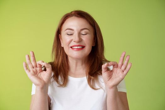 Close to perfection. Close-up peaceful relaxed redhead happy woman closed eyes pure delighted smile show zen peace satisfaction gesture meditating reach nirvana calm stand green background