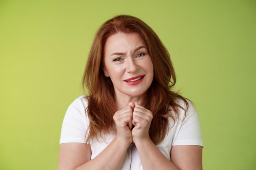 Silly touched tender redhead charmed middle-aged woman sighing gladly gaze admiration delighted press hands together heartwarmed fascinated look grateful lovely camera green background