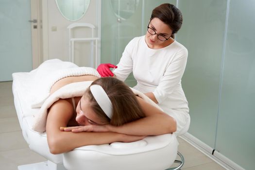 Young woman getting fat reductive skin lifting body treatment by a cosmetologist. Attractive female patient enjoying slimming body contouring procedure