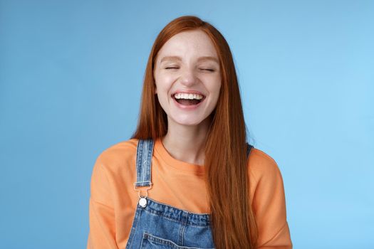 Carefree happy positive lucky redhead girl having fun close eyes smiling optimistic laughing out loud chuckling funny joke listen hilarious stories relaxing hang out friends, blue background