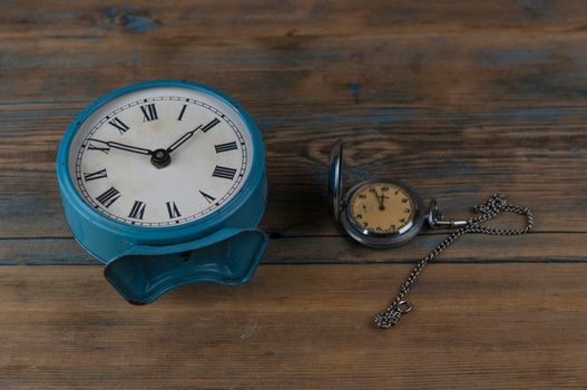 Alarm clock with roman numerals and vintage pocket watch on wooden table