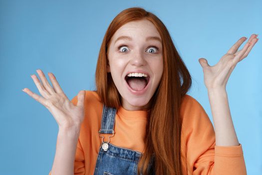 Surprised astonished sensitive overwhelmed young happy redhead girl receive incredible fantastic prize wide eyes astonished raising hands triumphing win lottery celebrating joyfully