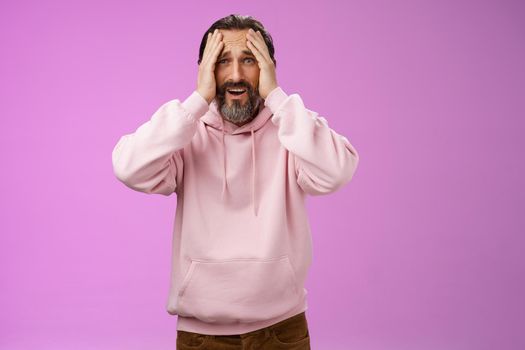Adult upset bearded man despair standing troubled concerned touching face frowning grimacing sorrow unhappiness, losing bet, was robbed, standing shocked devastated purple background, panic