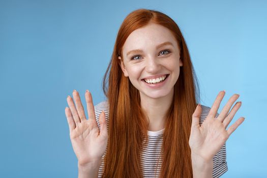 Charming redhead elder sister say goodbye sibling friends smiling cheerful waving raised palms show ten fingers grinning joyfully look carefree relaxed, talking casually blue background