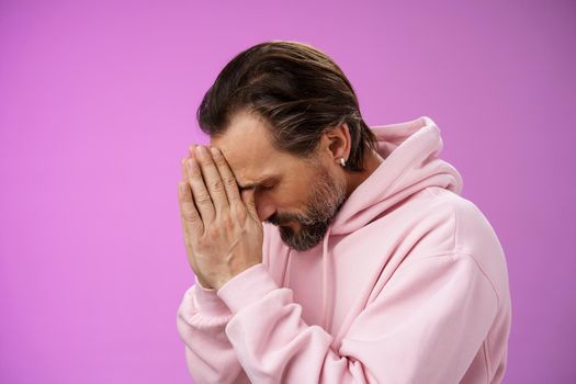 Concerned upset man supplicating asking god mercy help praying bow head close eyes hold hands pray hopefully waiting miracle worried wife health, standing sadness purple background