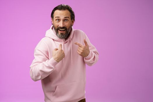 Excited surpried caucasian bearded guy pointing himself amazed questioned cannot believe was picked chosen standing thrilled purple background become winner lottery wearing pink hoodie.