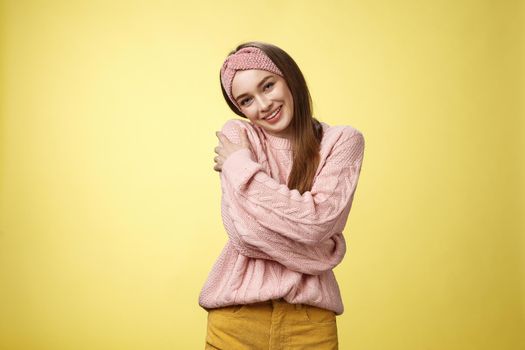 Girl feeling warm and safe thanks charming boyfriend embracing herself romantically hugging leaning on shoulder enjoying warmth of fluffy sweater, smiling tender in love over yellow background