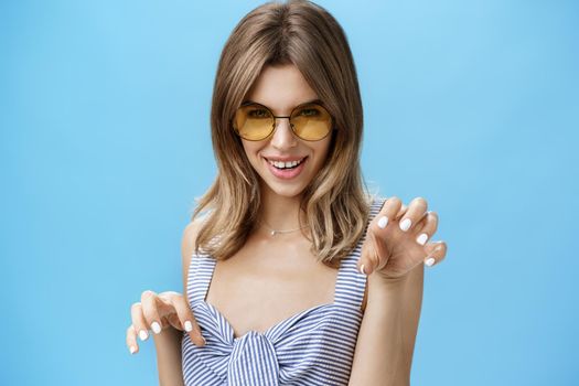 Sensual woman feeling like attractive wild cat raising hands like paws saying meow looking daring and flirty at camera, seducing with confident gaze, wearing stylish sunglasses and striped top