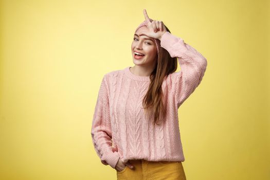 Attractive triumphing arrogant and confident cute glamourous woman in knitted sweater, headband showing l letter on forehead, loser sign and laughing over lost team, mocking having fun