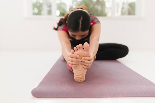 Young attractive yogi woman practicing yoga concept, sitting in Janu Sirsasana exercise, Head to Knee Forward Bend pose, working out wearing black sportswear, full length, white loft studio background
