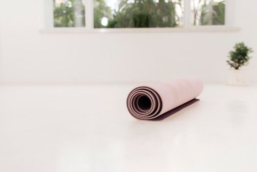 Rolled up yoga or pilates mat for exercise on natural wooden floor, sport class before or after practicing yoga, preparing for exercise