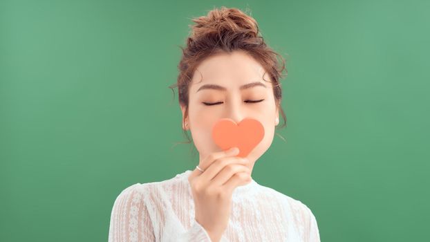Waist-up portrait of pretty Asian woman looking away with toothy smile while holding Valentines Day card in hands, white background