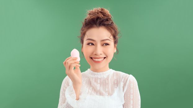 Woman applying foundation with beauty blender over green background