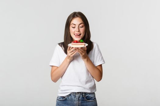 Portrait of tempted beautiful girl licking lips as looking at cake