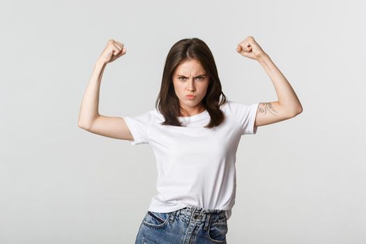 Serious-looking confident brunette girl flex biceps, showing strengths