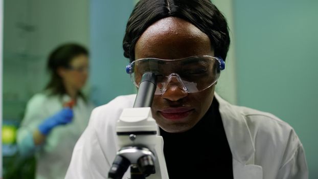 Closeup of african researcher woman looking at leaf slide under microscope