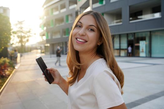 Side view of beauty happy woman looking at camera with phone in city