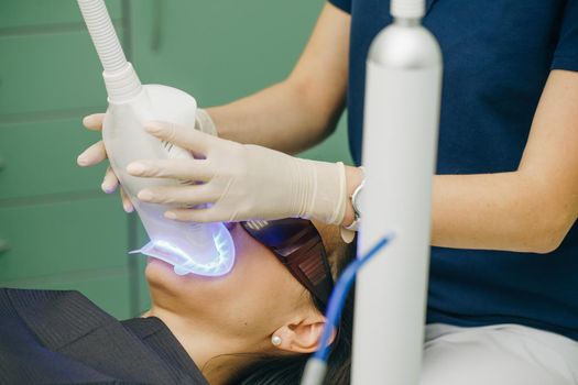 Teeth whitening procedure. Dentist stomatologist whitening teeth for patient in medicine dental clinic with lamp. Powerful light source is directed at patient's mouth to speed up the process.