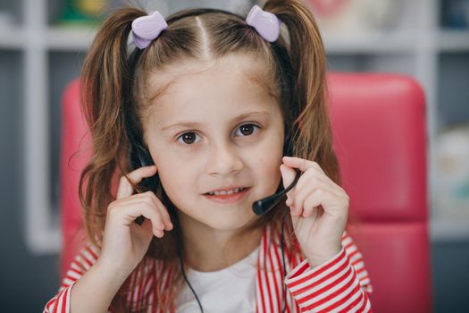 Portrait of smiling little girl wearing headphones. Happy small preschooler child in earphones have fun. Studying online on quarantine.