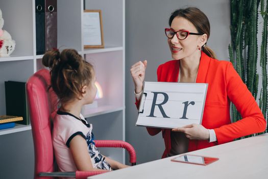 Speech therapist teaches the girls to say the letter R. Speech therapist holding letter R and girl back view