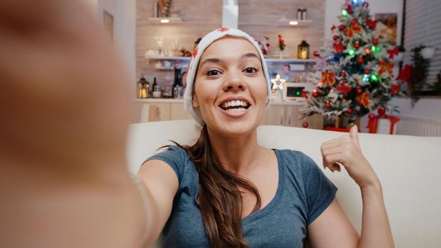 POV of festive woman using video call communication to celebrate christmas eve with family on online remote conference. Person wearing santa hat talking on webcam for holiday celebration