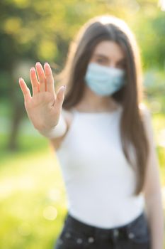 Vertical Portrait of a young woman wearing protective mask makes stop sign with hand, saying no, expressing restriction. Concept health and safety, N1H1 coronavirus quarantine, virus protection