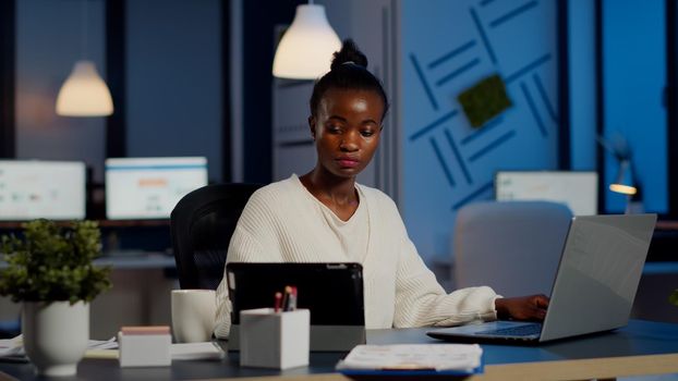 Multitasking black business woman working at laptop and tablet in same time