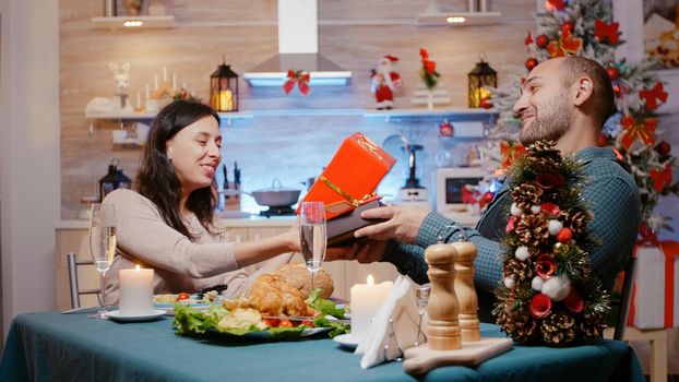 Festive couple exchanging gift boxes at christmas eve dinner