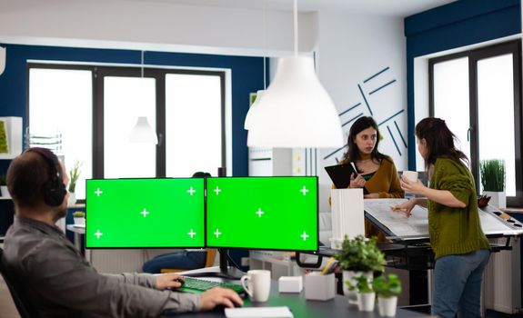 Employee with headphones working in dual monitror setup with green screen