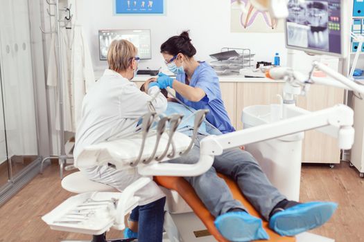 Sick man lying on stomatological chair while senior doctor taking care of tooth health