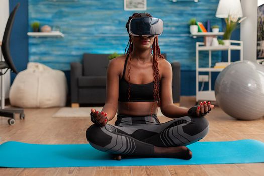 Calm tranquil black woman wearing vritual reality goggles sitting on yoga mat