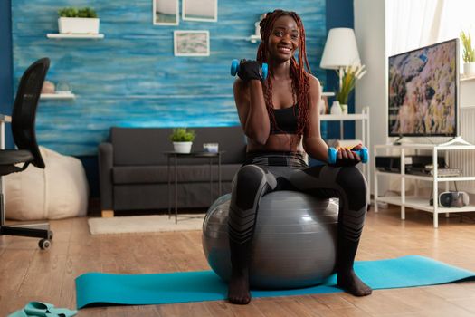 Joyful athletic black person in leggings sportwear using stability ball for training