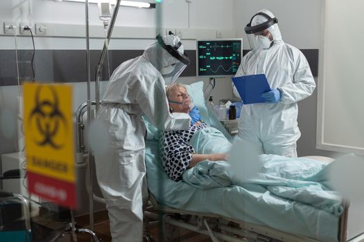 Medical nurse dressed in ppe suit putting oxygen mask to senior patient