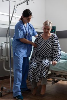 Medical nurse in scrubs helping senior woman in hospital room