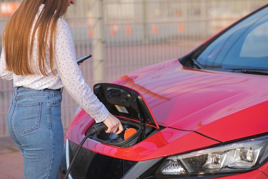Woman Hand Attaching Power Cable To Environmentally Friendly Zero Emission Electric Car. Woman makes power supply plugged into an electric car being charged.