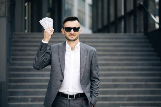 Lifestyle, richness, joy, success. Happy rich successful man holds dollars outdoors. Portrait of satisfied businessman holds money.