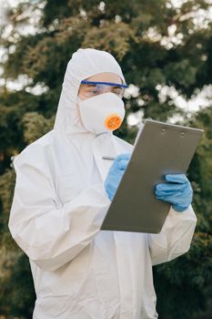 Doctor epidemiologist fighting with coronavirus COVID-19. Coronavirus Protection Pandemic Threat Covid 19. Woman in a Protective Insulating Suit and Mask notes the Data in a Notebook.