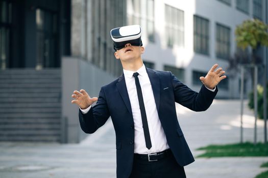 Handsome man wearing virtual reality headset. Augmented Reality. Businessman touch something using modern 3D vr glasses near office building. This new technology offers new 3D dimensions