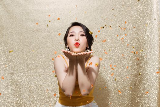 Portrait of a pretty woman blowing confetti from her hands isolated over sparkles background