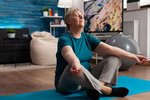 Senior woman sitting comfortable in lotus position on yoga mat with closed eyes