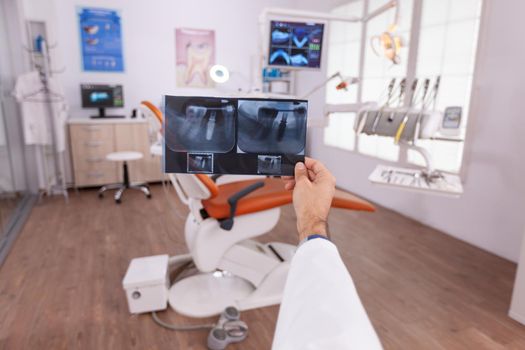 Specialist radiologist analyzing tooth dental medical radiograph working in stomatology diagnosis hospital office room. In background empty orthodontic cabient preparing for oral teeth examination