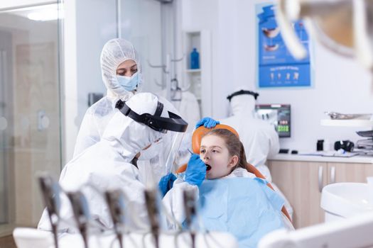 Dental specialist in ppe suit checking child cavity