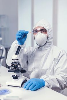 Microbiologist dressed in ppe suit analyzing sample on microscope glass slide