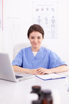 Portrait of healthcare nurse smiling looking at camera while using laptop in hospital office. Medical practitioner using notebook in clinic workplace , confident, expertise, medicine.